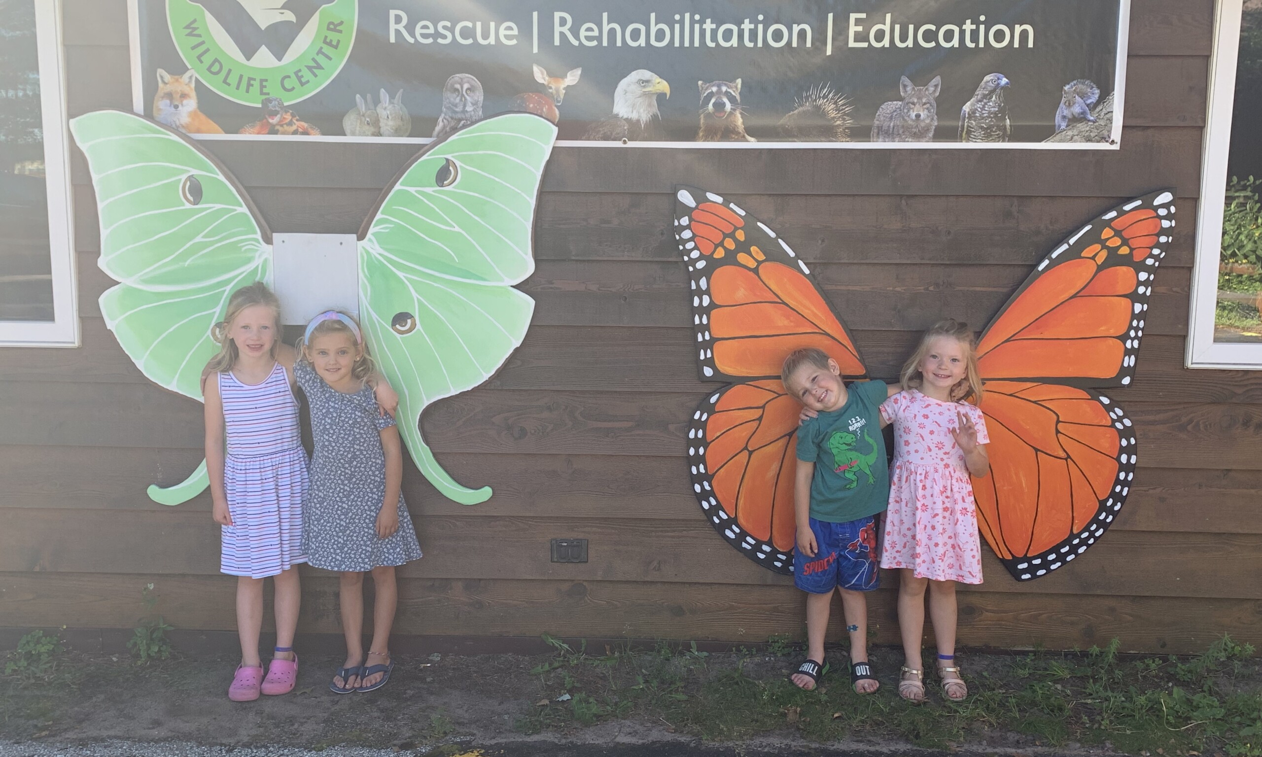 children standing in front of wooded butterfly wings while on a tour 