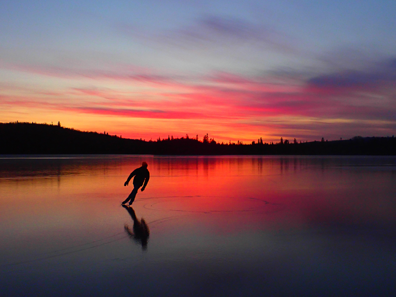 An ice skater carving elegant lines and a perfectly smooth lake against a warm sunset